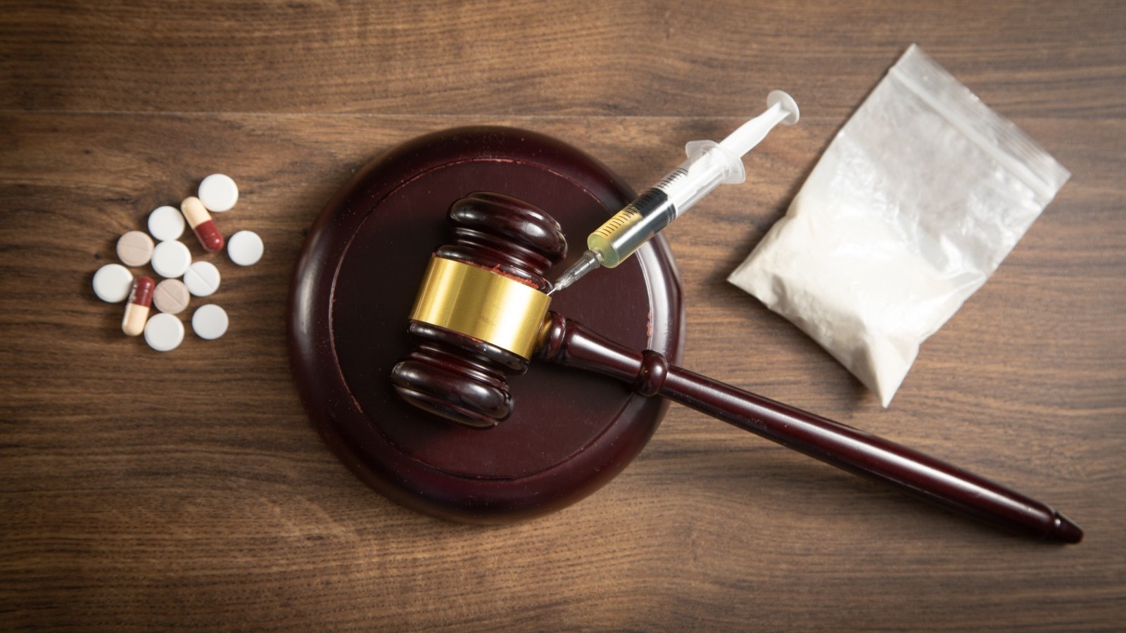 A gavel beside pills, a syringe and a bag of powder.